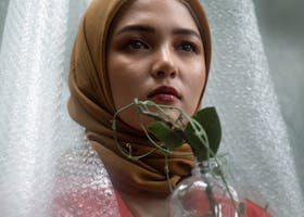 Elegant portrait of a woman in hijab holding a plant, showcasing beauty and tradition.